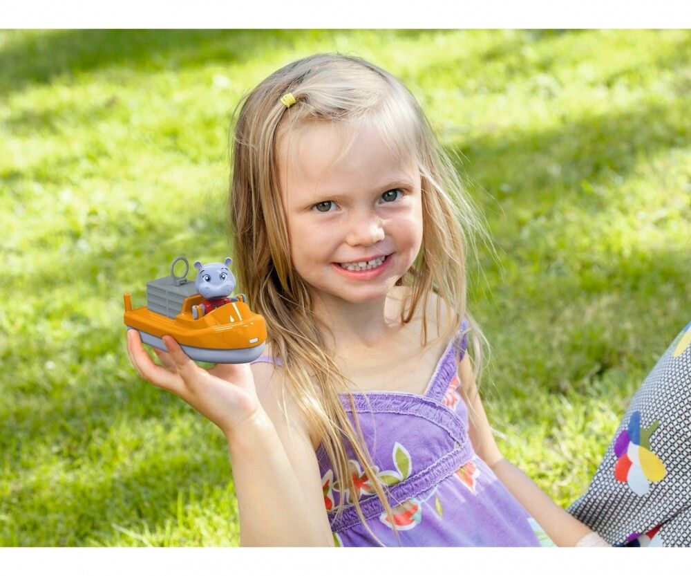 Ein Mädchen hält ein orangefarbenes Boot mit einem Nilpferd-Kapitän. Sie lächelt in die Kamera, im Hintergrund Gras.