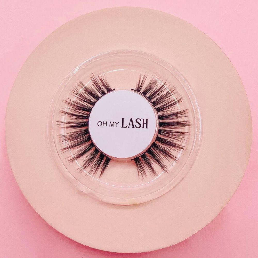 Falsche Wimpern auf rosa Untergrund. Runde, transparente Verpackung. Aufschrift "OH MY LASH".