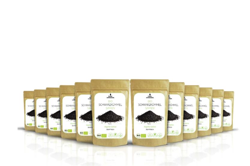 Reihe von Beuteln mit Bio-Schwarzkümmel Samen. Braune Verpackung mit weißem Etikett und Produktbezeichnung. Bio-Siegel.