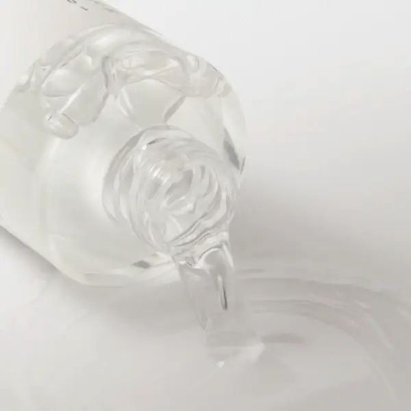 Transparente Flüssigkeit fließt aus einer Flasche. Weißer Hintergrund.