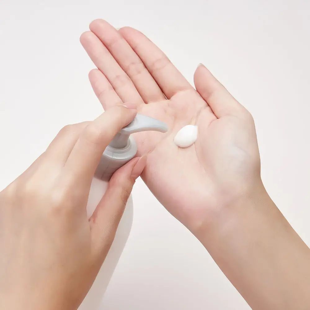 Hände halten eine Pumpe und einen Klecks Creme. Weiße Creme in der Handfläche. Heller Hintergrund.