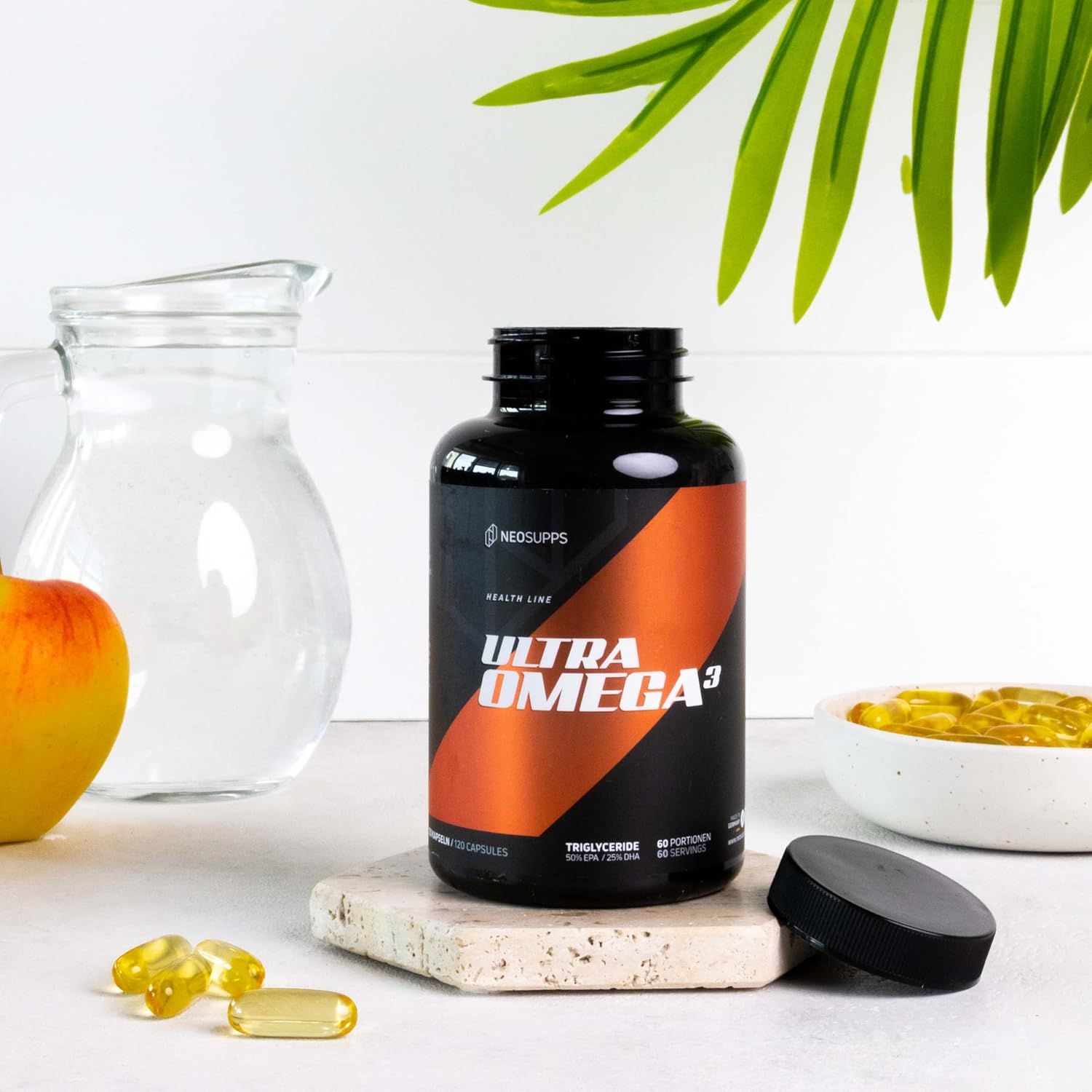 Schwarze Flasche mit orangefarbenem Etikett. Text: Ultra Omega 3. Kapseln und Glasgefäß daneben. Deckel liegt daneben.