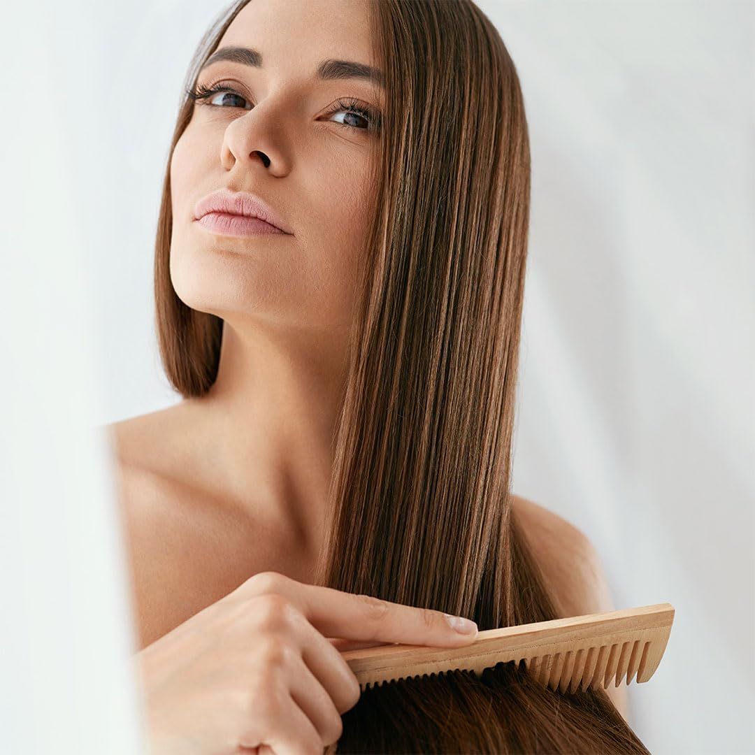 Frau mit langen, braunen Haaren, die sie mit einem Holzkamm kämmt.