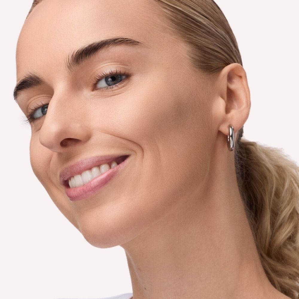 Porträt einer Frau mit hellem Teint. Sie trägt Ohrringe. Ihr Gesicht ist leicht konturiert.