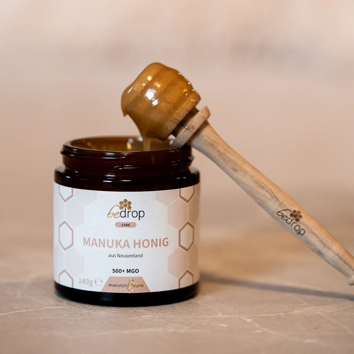 Glas Manuka Honig mit Löffel. Honig tropft in das Glas. Etikett mit Produktinformationen.