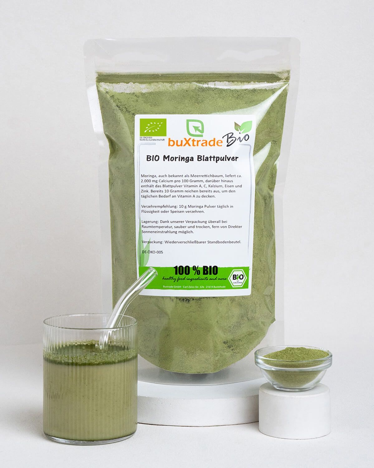 Verpackung mit Moringa-Pulver, daneben ein Glas mit Getränk und eine Schale mit Pulver.