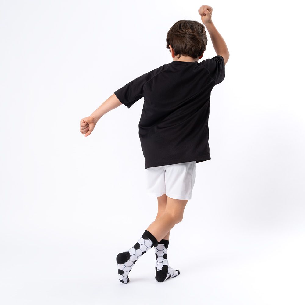 Junge von hinten, jubelt. Schwarzes T-Shirt, weiße Shorts. Socken mit Fußballmuster, schwarz-weiß.