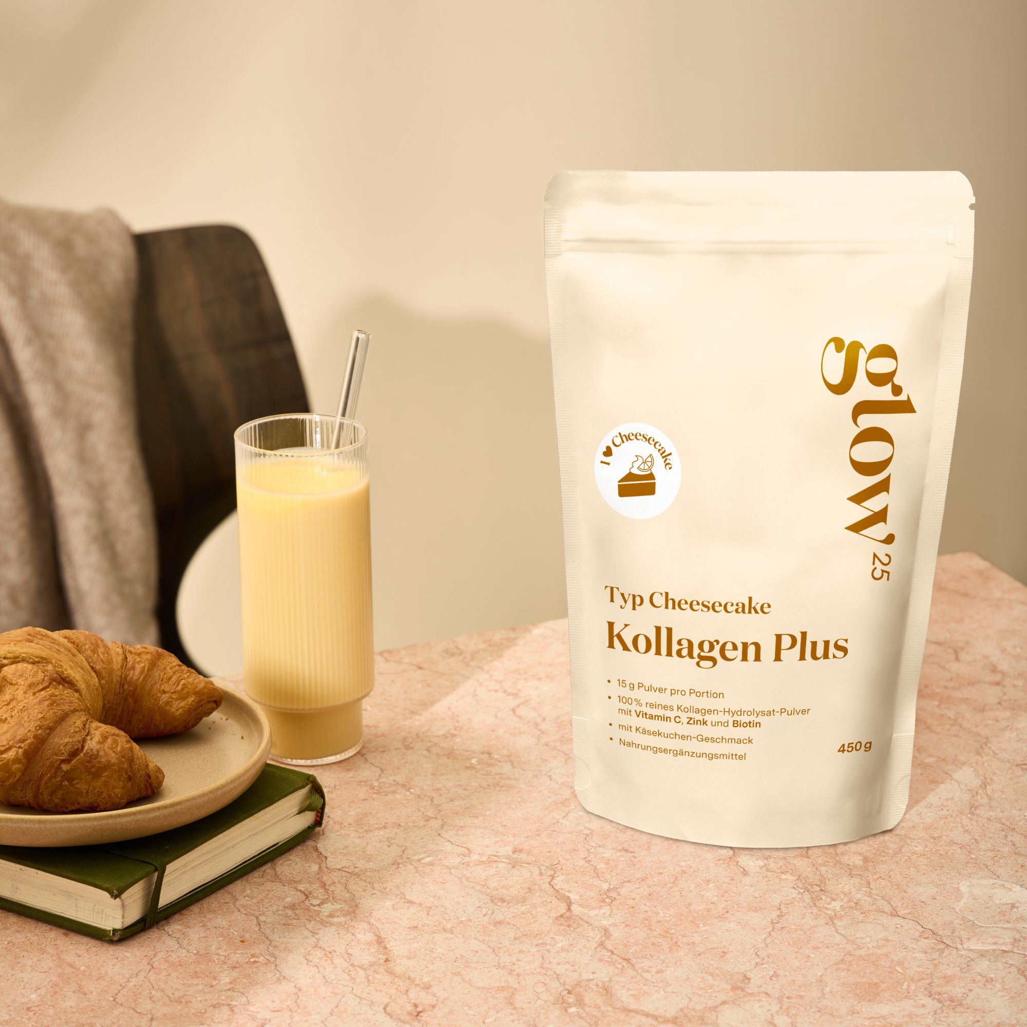 Glow25 Typ Cheesecake Kollagen Plus Beutel neben Glas mit Getränk und Croissant auf Teller. Auf Tisch mit Buch.