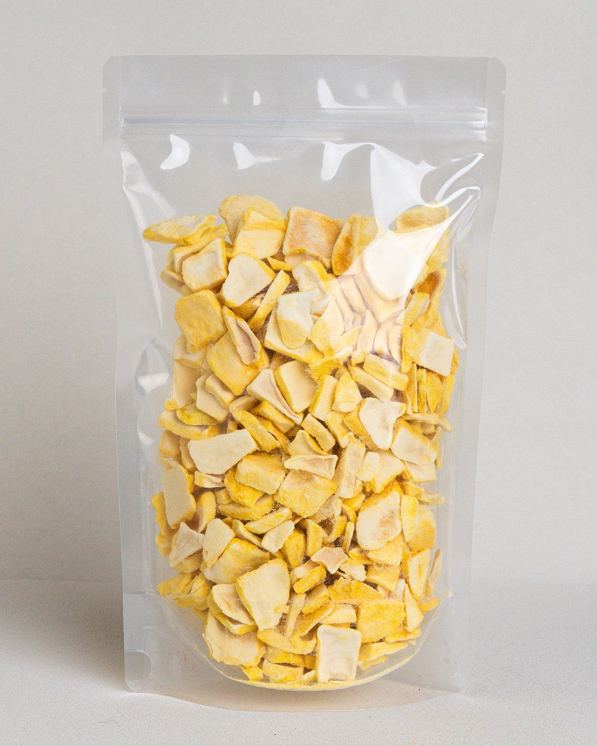 Transparente Verpackung mit gefriergetrockneten Mangoscheiben. Die Scheiben sind gelb und unregelmäßig geformt.