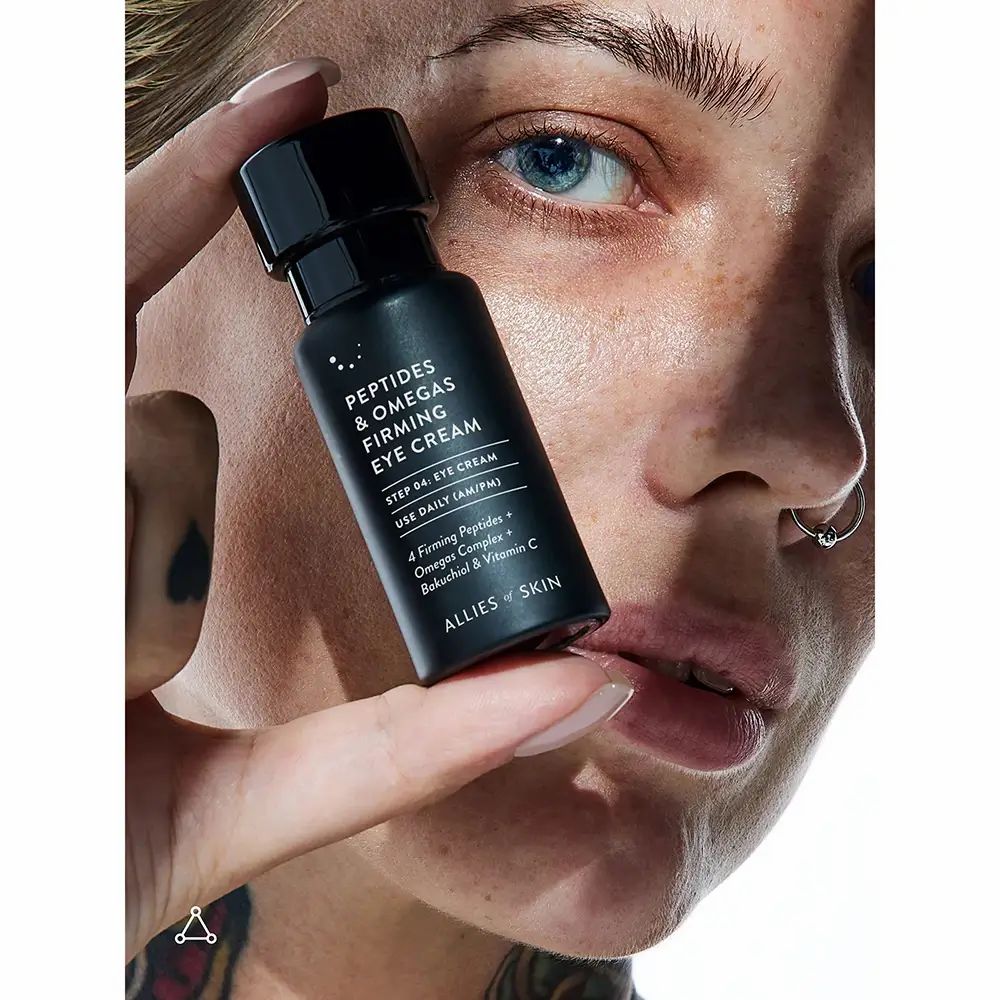 Person hält eine schwarze Flasche. Text: Peptides & Omegas Firming Eye Cream. ALLIES OF SKIN.