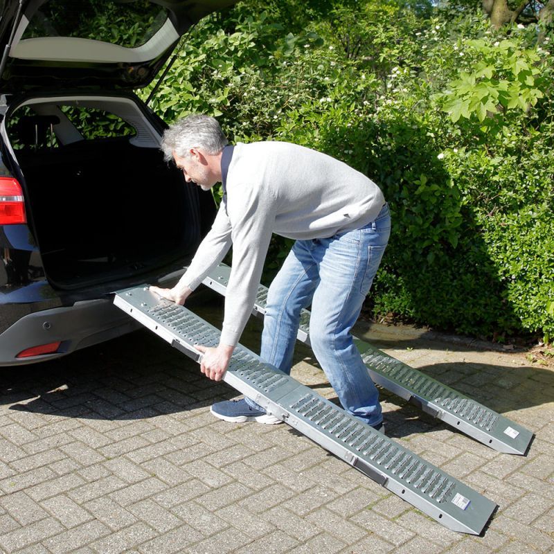 Mann benutzt zwei silberne Auffahrrampen, um etwas in einen Kofferraum zu laden. Rampen sind ausgeklappt.