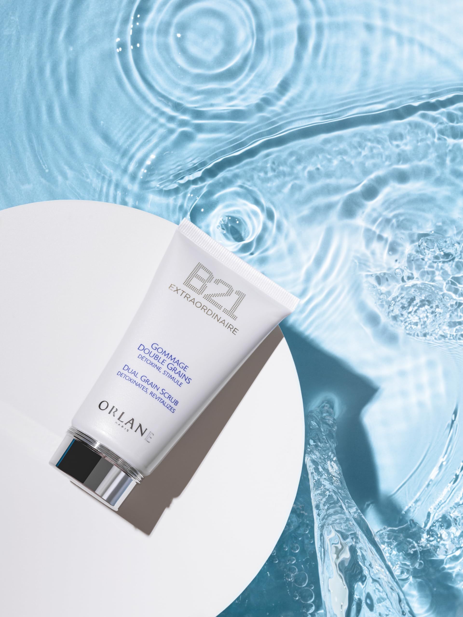 Weiße Tube mit 'B21 Extraordinaire' und 'Gommage Double Grains' Schriftzug. Auf Wasserhintergrund.