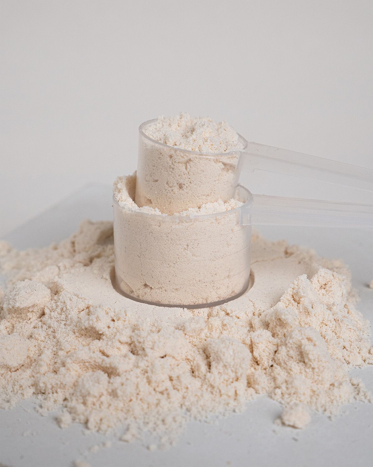 Zwei Messlöffel mit Proteinpulver. Pulver liegt verstreut. Auf weißem Untergrund.