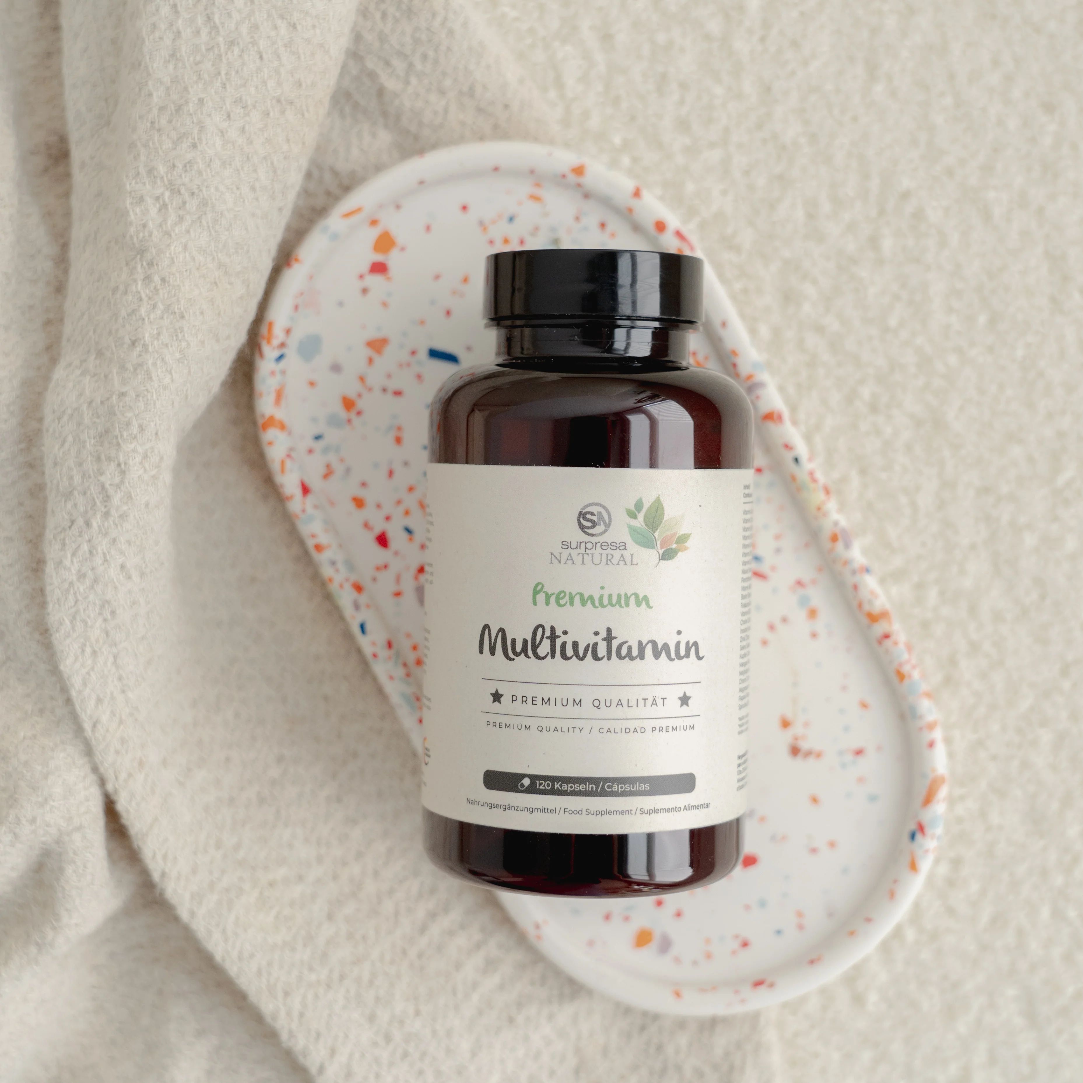 Braune Flasche mit Etikett auf Tablett und Tuch. Aufschrift: Surpresa Natural Multivitamin. Schwarzer Deckel.