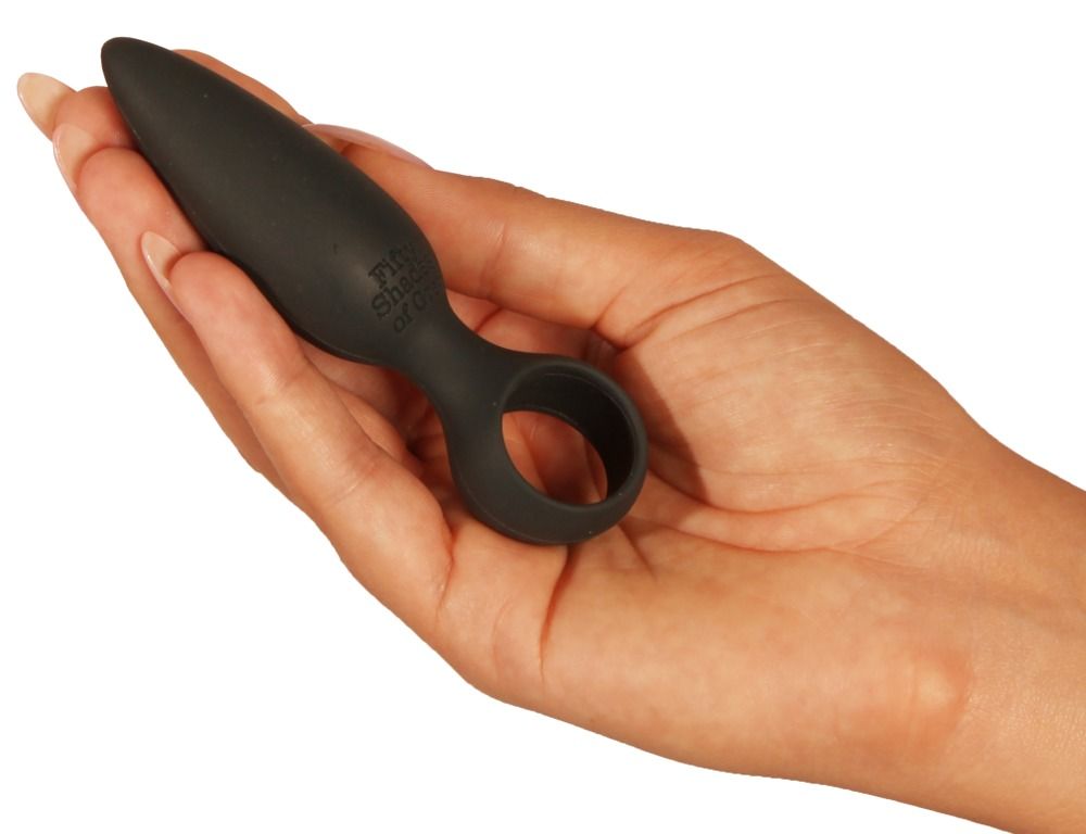 Schwarzer Analplug in Hand gehalten. Aufschrift "Fifty Shades of Grey". Kegelförmiger Kopf, Ring an der Basis.