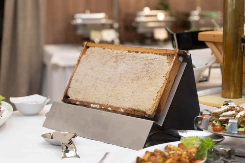 Honigwabe in Holzrahmen auf einem Buffet. Präsentiert auf einem Ständer. Umgebung: Speisen, Besteck.
