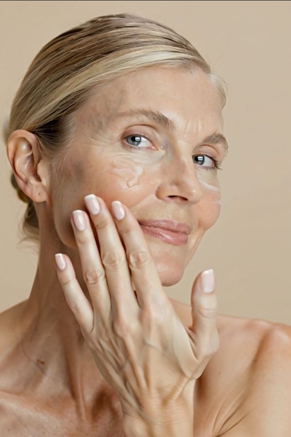 Frau trägt Creme auf ihr Gesicht auf. Sie lächelt. Creme ist sichtbar auf der Haut.