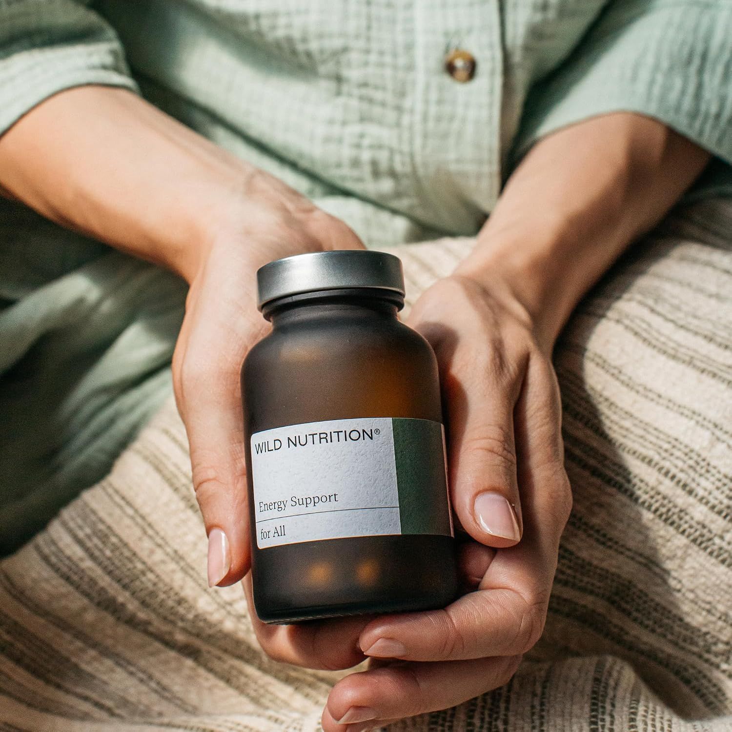 Hände halten eine braune Glasflasche mit Etikett 'Wild Nutrition', Energie-Unterstützung.
