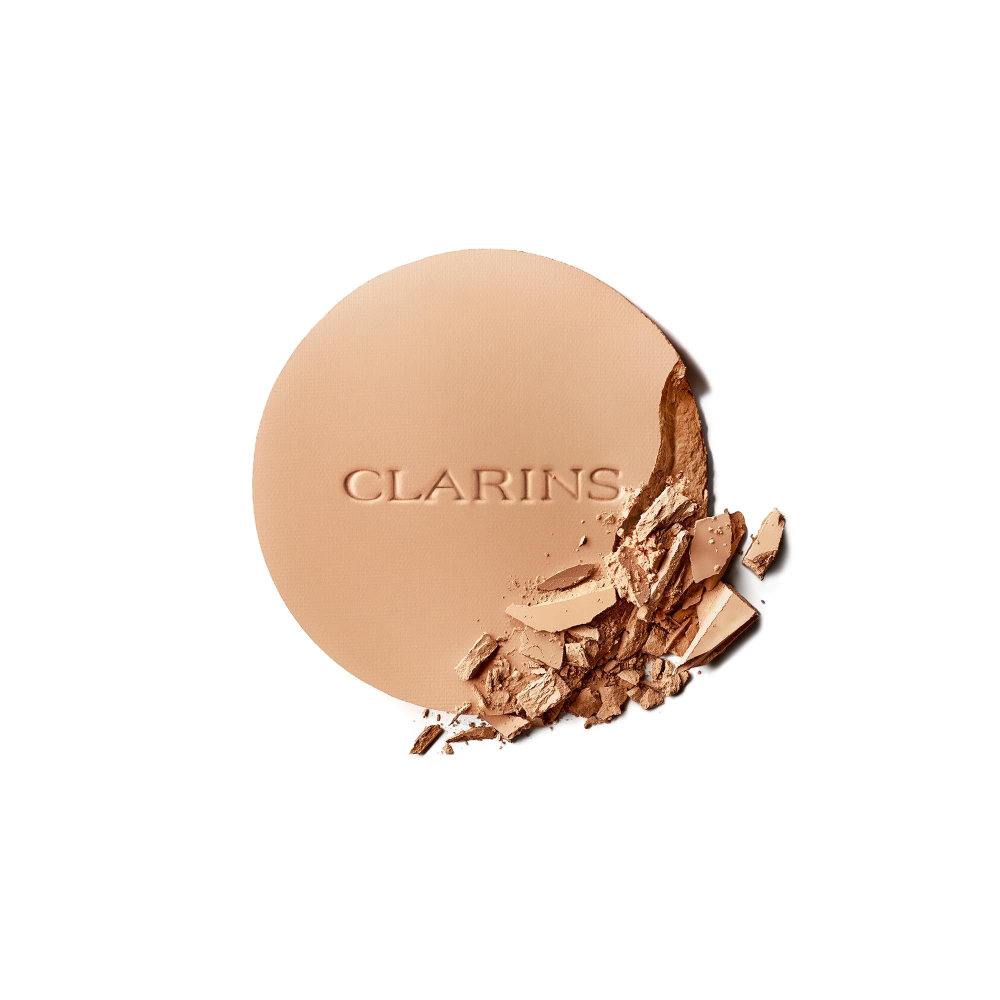 Kompaktpuder mit CLARINS-Logo. Teilweise zerbrochen, zeigt die Textur. Runde Form, helle Farbe.