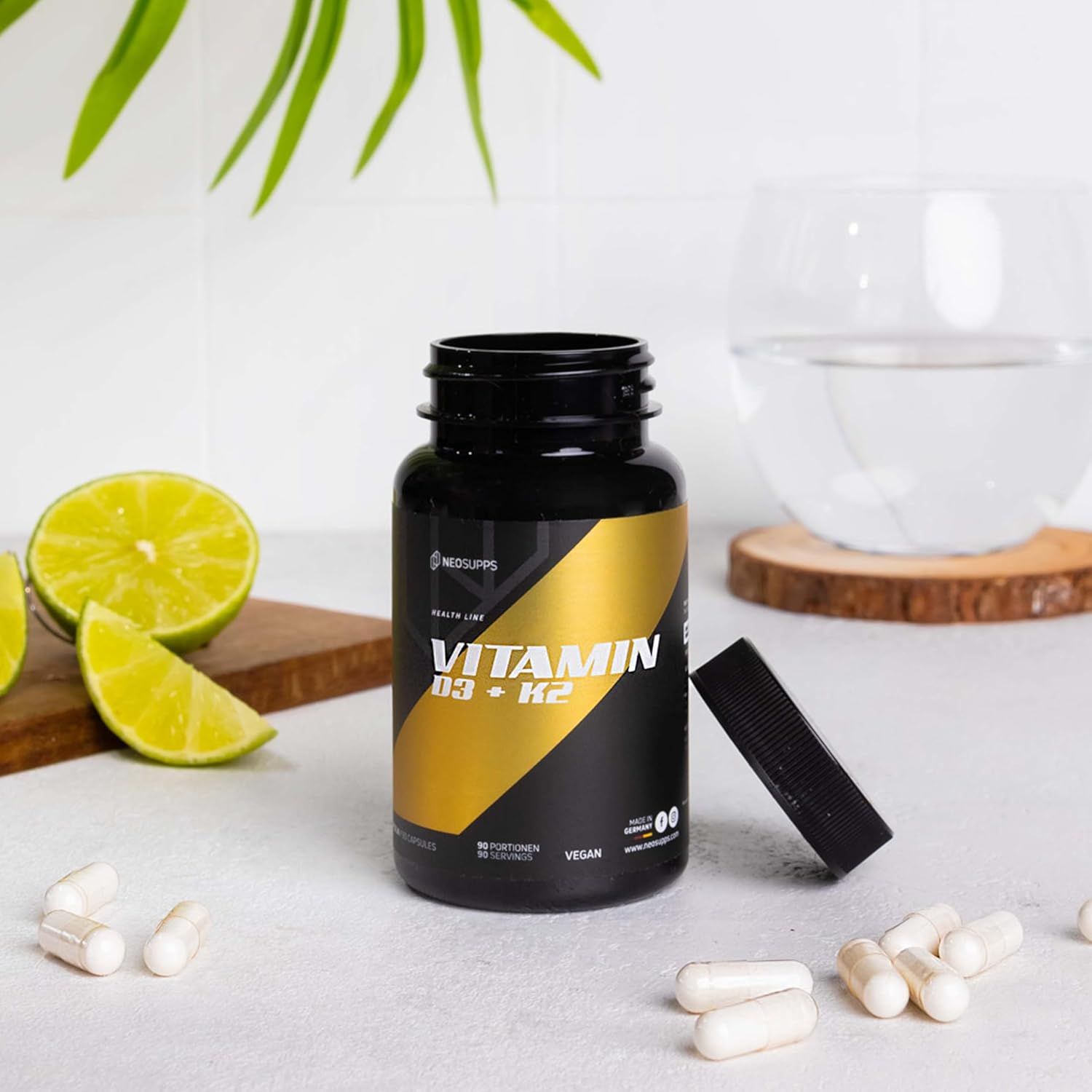 Schwarze Flasche mit goldfarbenem Etikett. Aufschrift Vitamin D3 + K2. Daneben Kapseln und eine Limette.