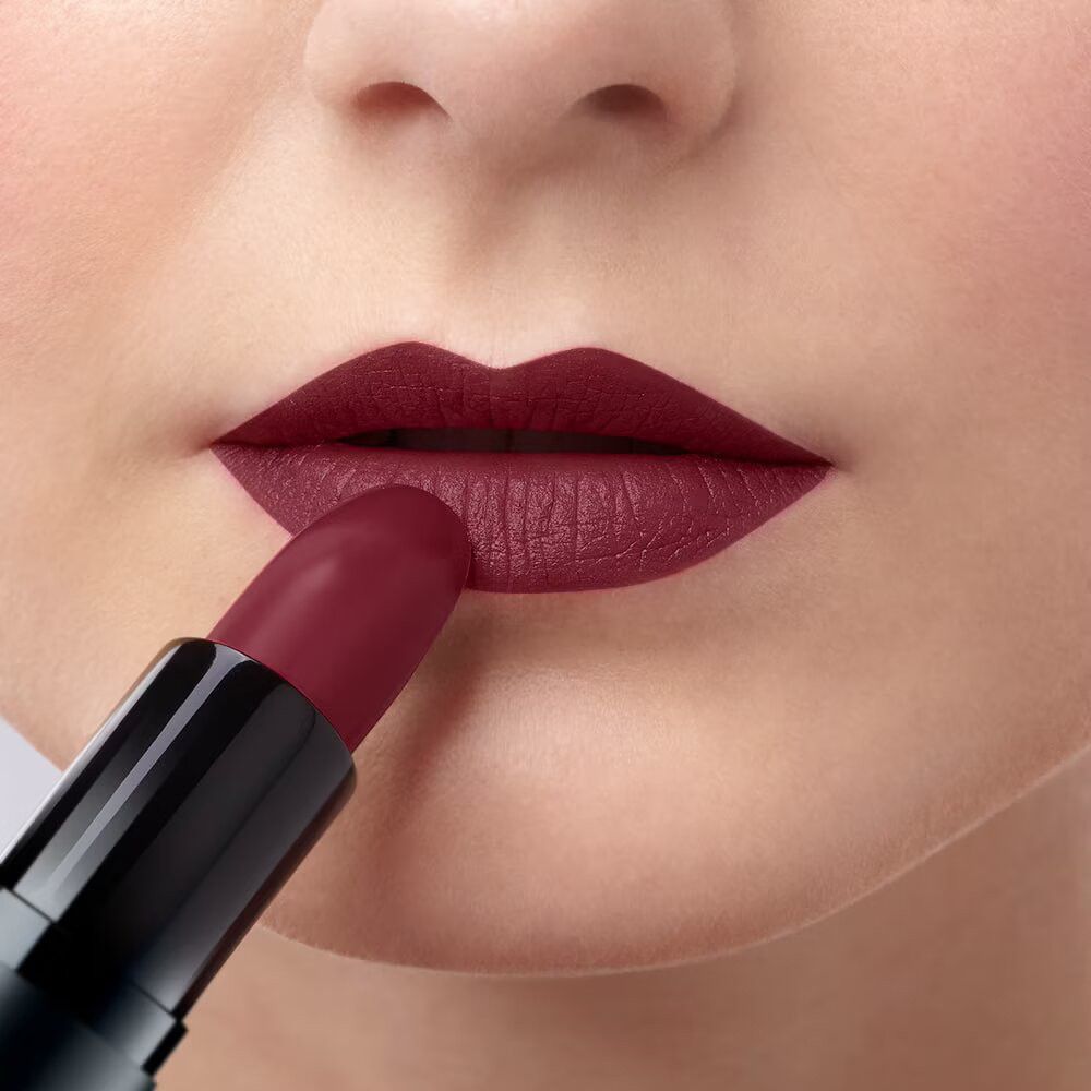 Person, die Lippenstift auf die Lippen aufträgt. Dunkelroter Lippenstift. Nahaufnahme.