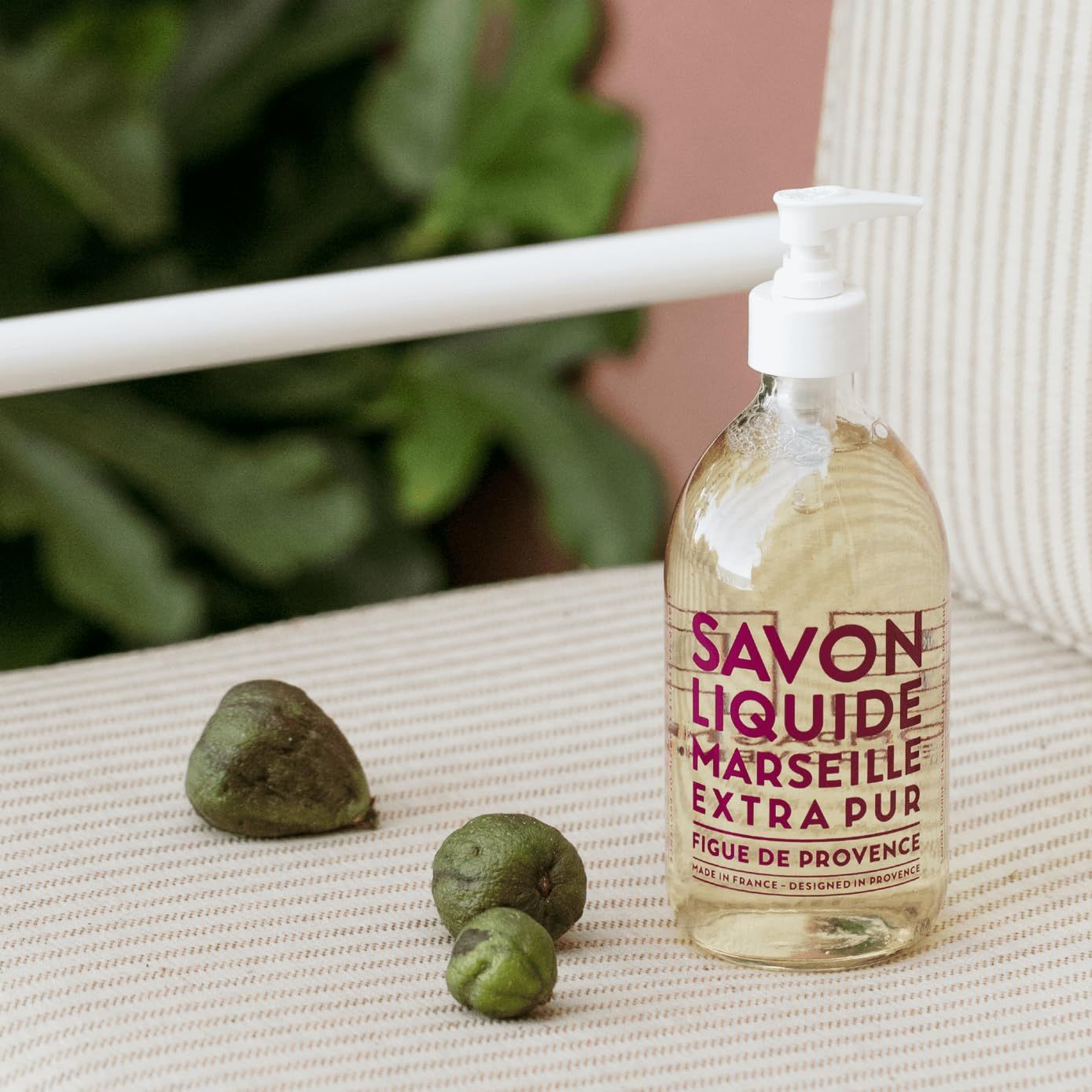 Flüssigseife mit Pumpe neben Feigen auf einem Stuhl. Aufschrift SAVON LIQUIDE MARSEILLE EXTRA PUR Figuier de Provence.