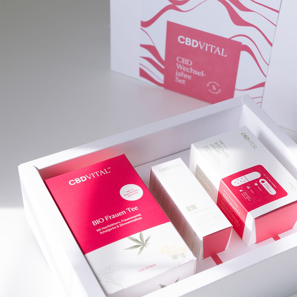 Geschenkbox mit CBD Vital Produkten. Enthält Tee, Tropfen und Kapseln in einer weißen Box. Rote Verpackungen mit Logo.