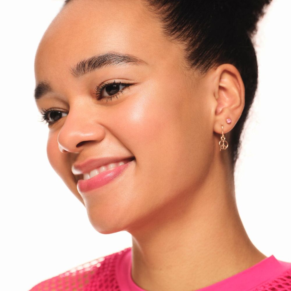 Porträt einer lächelnden Frau. Haut mit Highlighter betont. Goldene Ohrringe mit Peace-Zeichen.