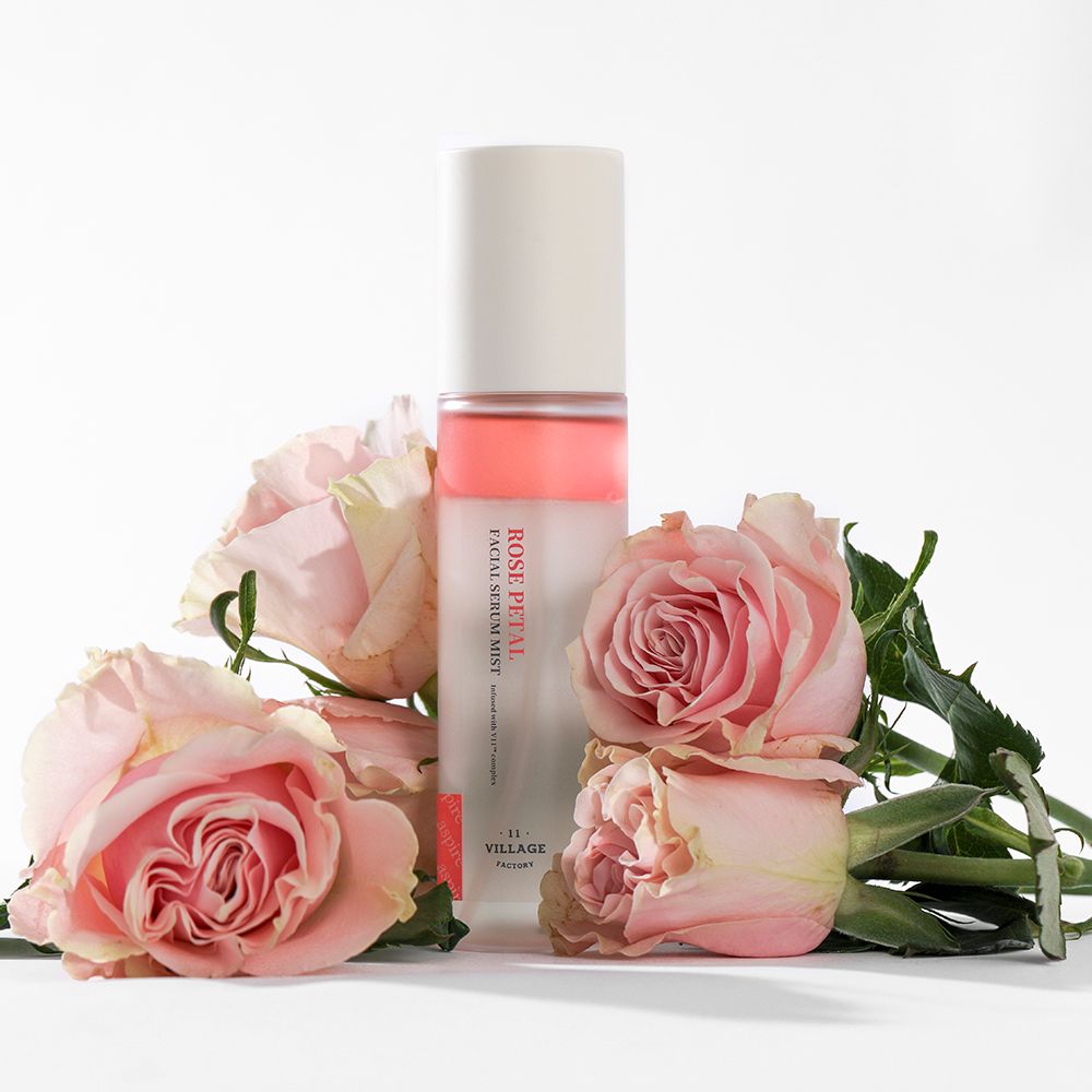 Gesichtsserum-Nebel mit Rosen. Flasche mit rosa Flüssigkeit. Text: ROSE PETAL FACIAL SERUM MIST. Marke: VILLAGE 11 FACTORY.