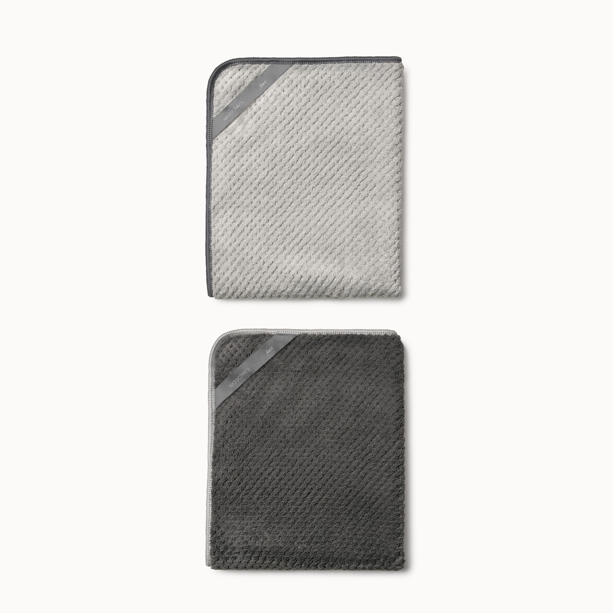 Zwei rechteckige Mikrofasertücher. Oben hellgrau, unten dunkelgrau. Beide mit dunkelgrauen Rändern und diagonalem Band.