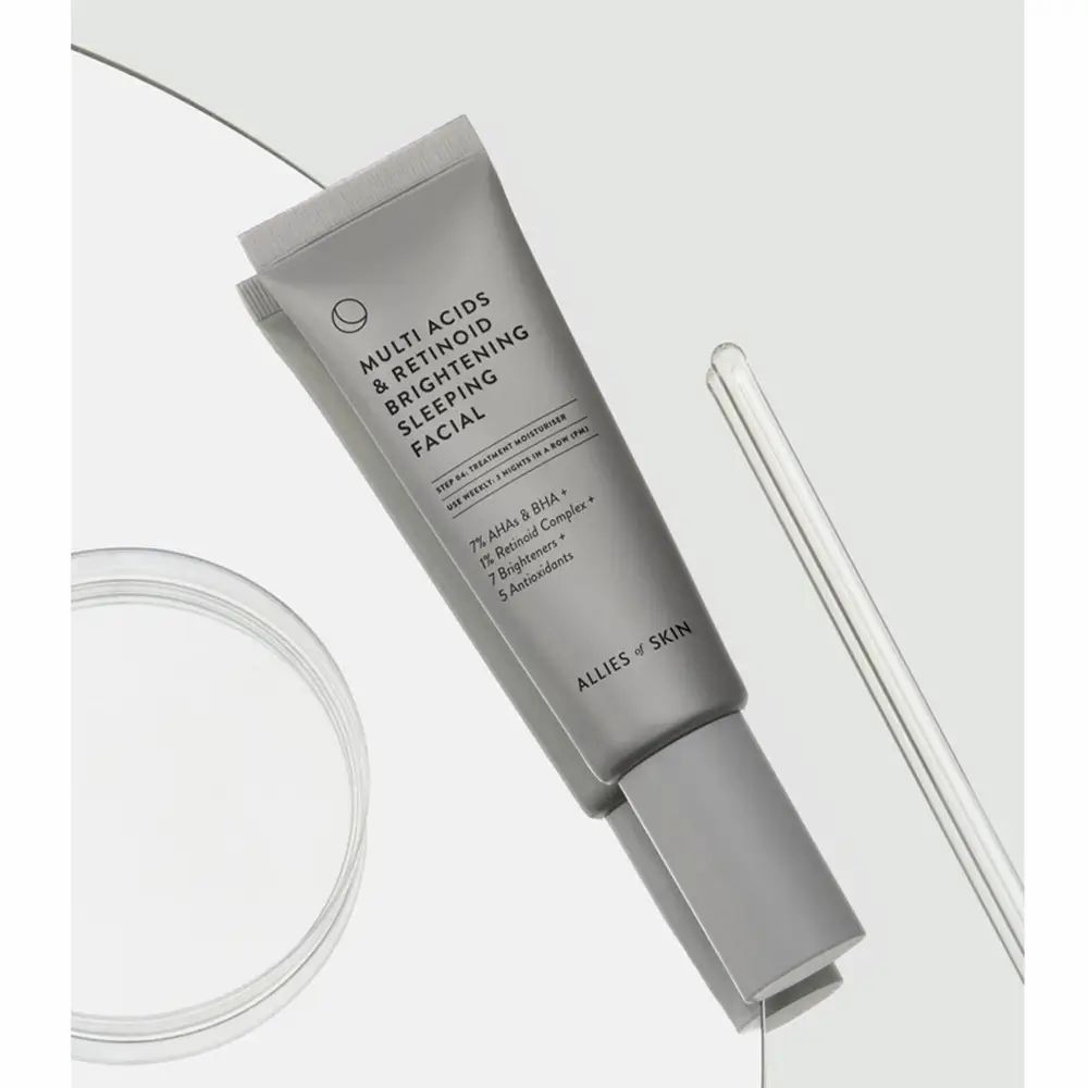Graue Tube mit Produkttext. Aufschrift: Multi Acids & Retinoid. Marke: Allies of Skin. Auf Glasplatte platziert.
