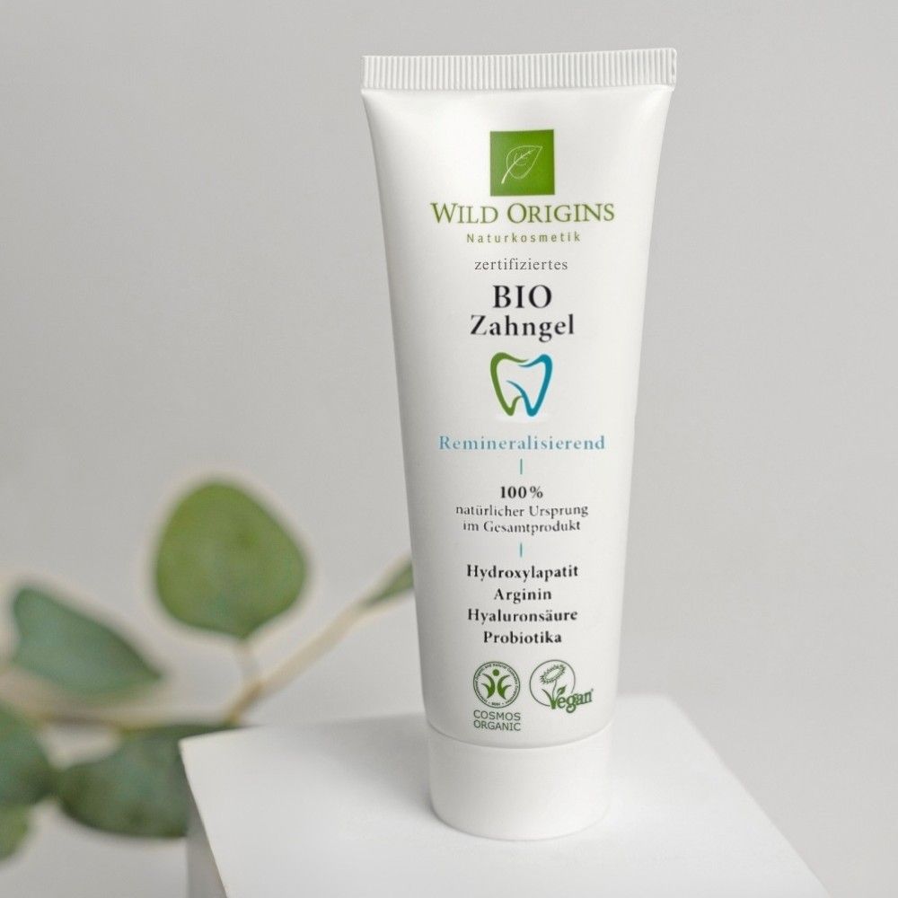 Weiße Tube mit grünem Logo und Schriftzug BIO Zahngel. Auf weißer Oberfläche. Vegan-Siegel und Cosmos Organic-Siegel.