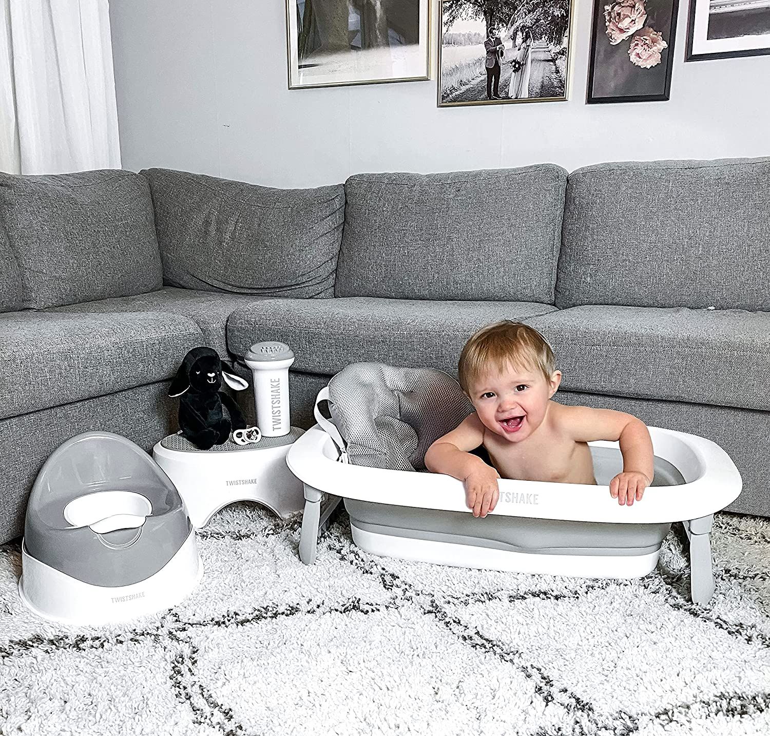 Kleinkind in Badewanne mit Badekissen. Graue Badewanne, graues Sofa, Teppich.