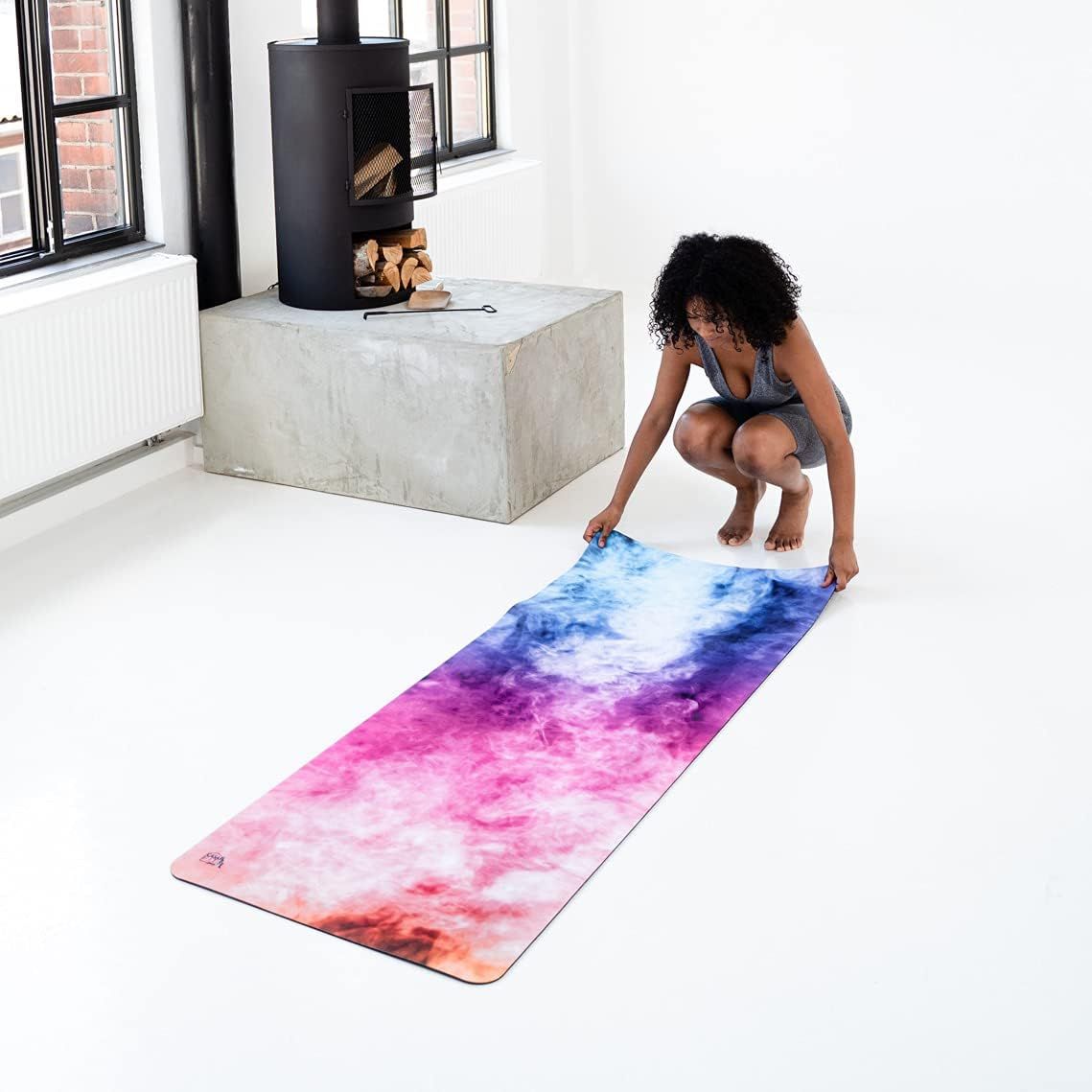 Frau rollt Yogamatte aus. Pink-blaue Matte auf weißem Boden. Kamin im Hintergrund.