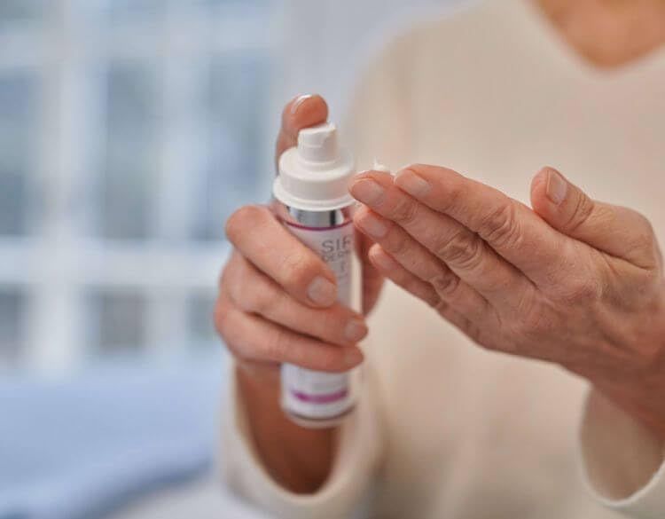 Eine Hand hält einen weißen Pumpspender mit silbernem Akzent. Eine andere Hand empfängt eine kleine Menge Serum.