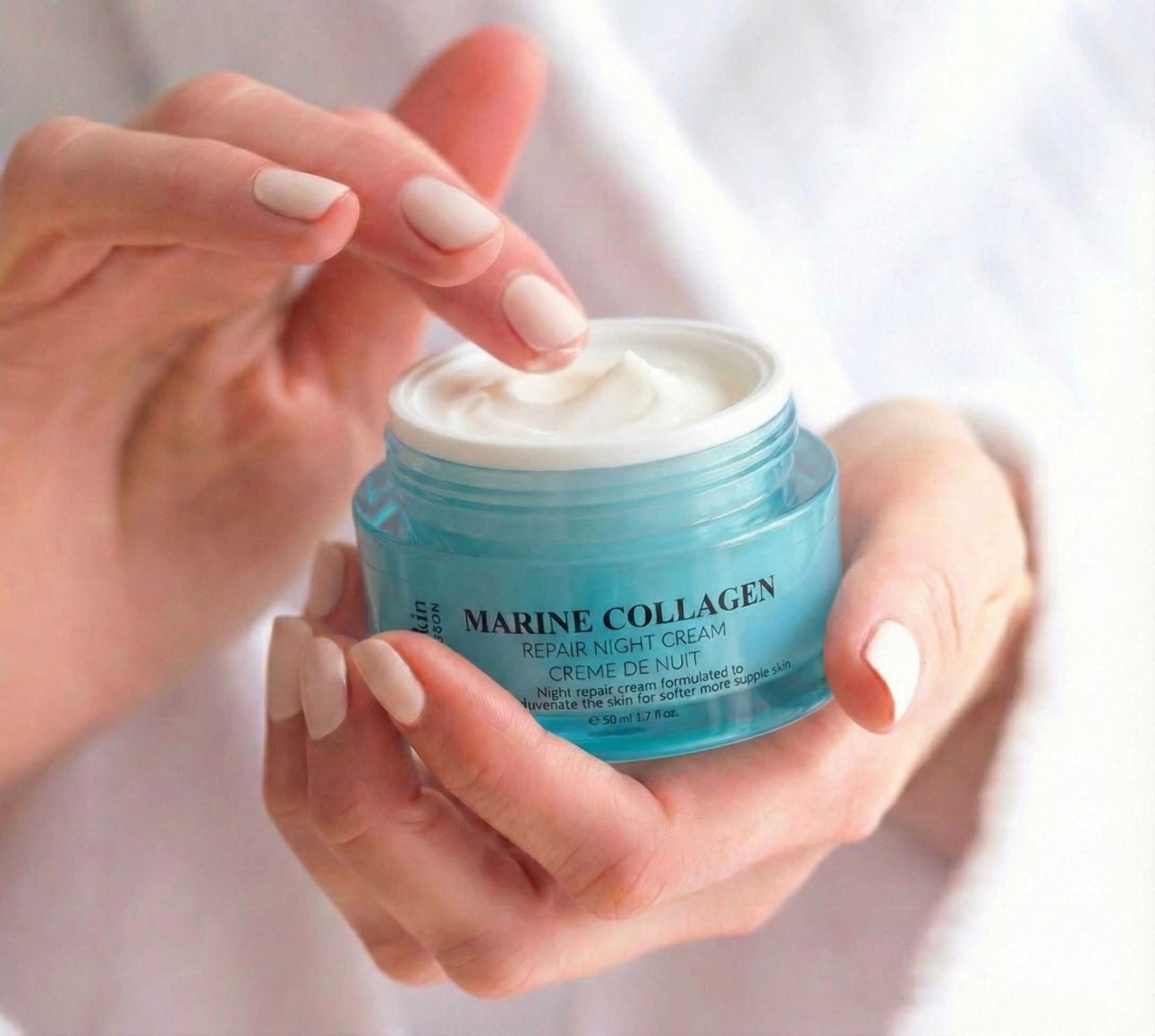 Hände halten einen Tiegel Marine Collagen Nachtcreme. Creme wird mit dem Finger entnommen. Blaues Glas, silberner Deckel. Text: Marine Collagen.