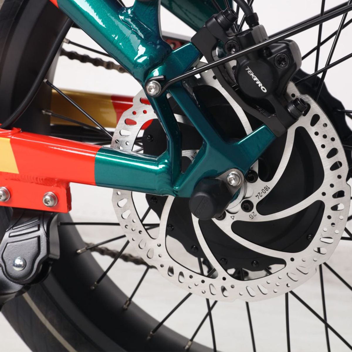 Hinterradbremse eines E-Bikes. Scheibenbremse, schwarze Details. Grün-rotes Design. TEKTRO-Logo sichtbar.