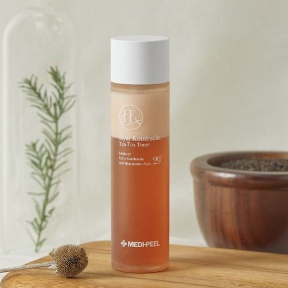 Hyal Kombucha Tea-Tox Toner Flasche auf Holzbrett, neben Pflanzen und Schale.