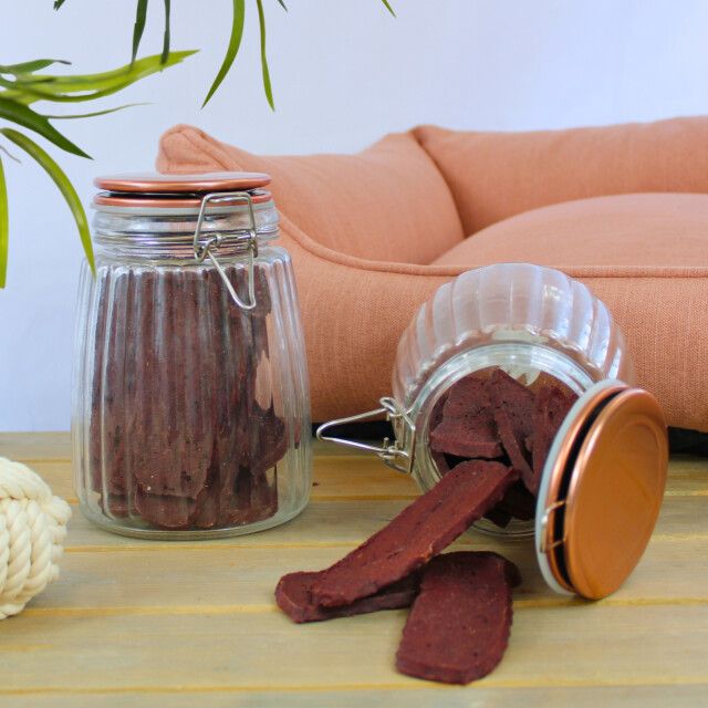 Zwei Gläser mit Rindfleischstreifen, eines offen. Deckel mit braunen Rändern. Auf Holzoberfläche.