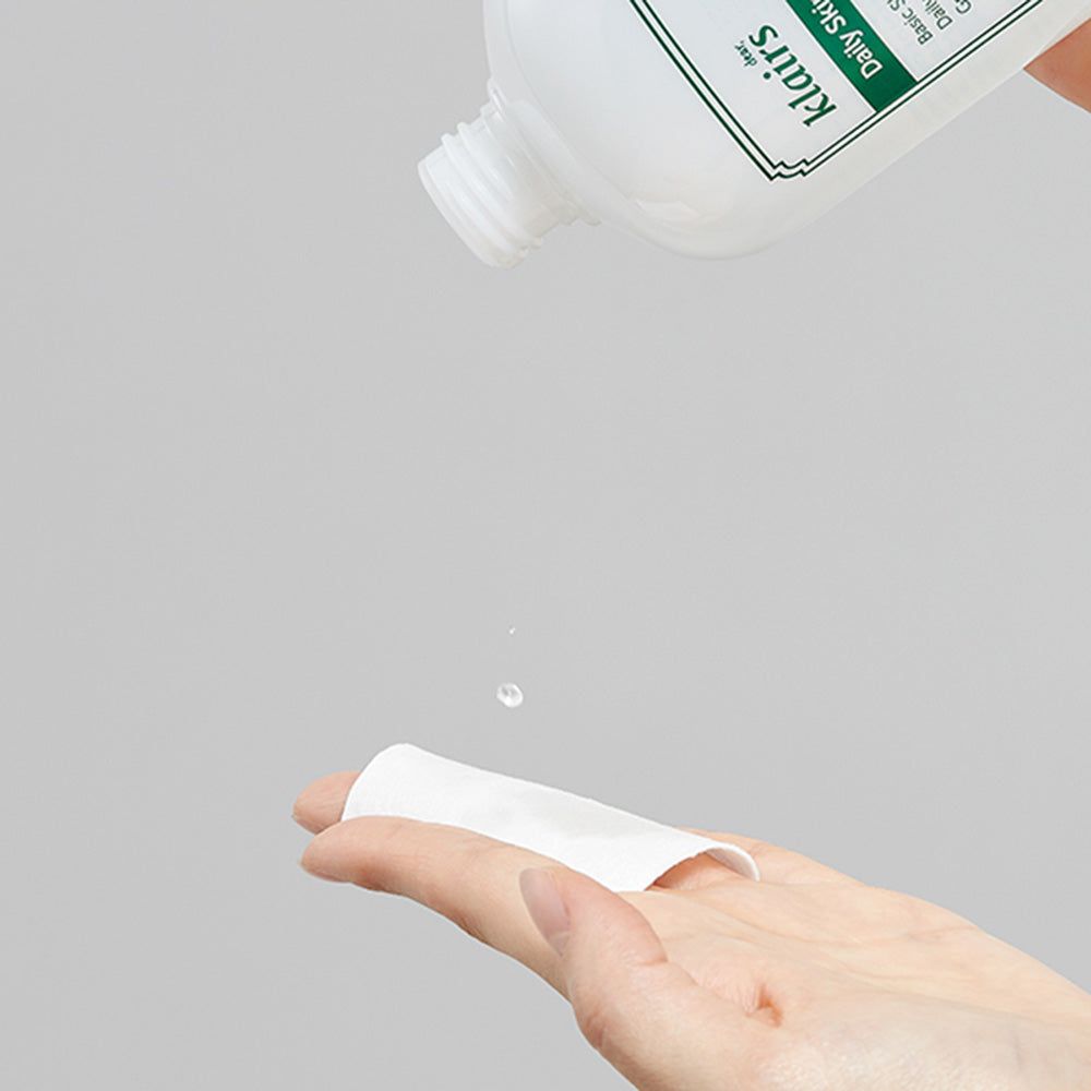 Weiße Flasche mit grünem Etikett. Text: "klairs Daily Skin Hydrating Water". Flüssigkeit tropft auf Wattepad.