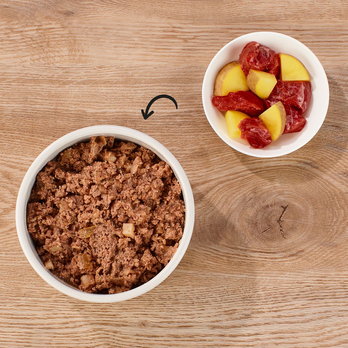 Zwei Schalen mit Hundefutter. Eine Schale mit Fleisch, die andere mit Kartoffeln und Fleischstücken. Auf Holzuntergrund.