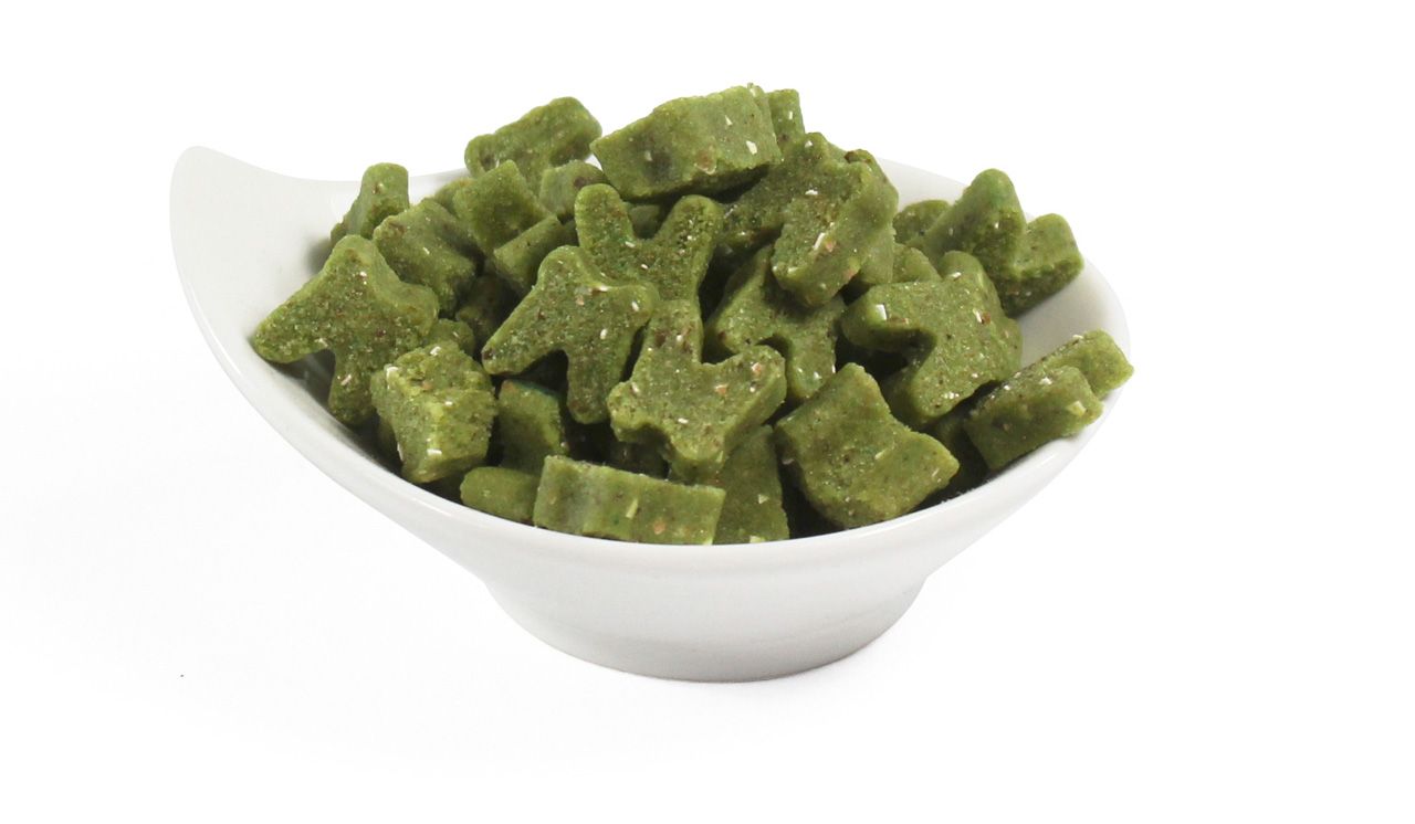 Grüne, sternförmige Snacks in einer weißen Schale. Einige Snacks sind zerkleinert. Auf hellem Hintergrund.