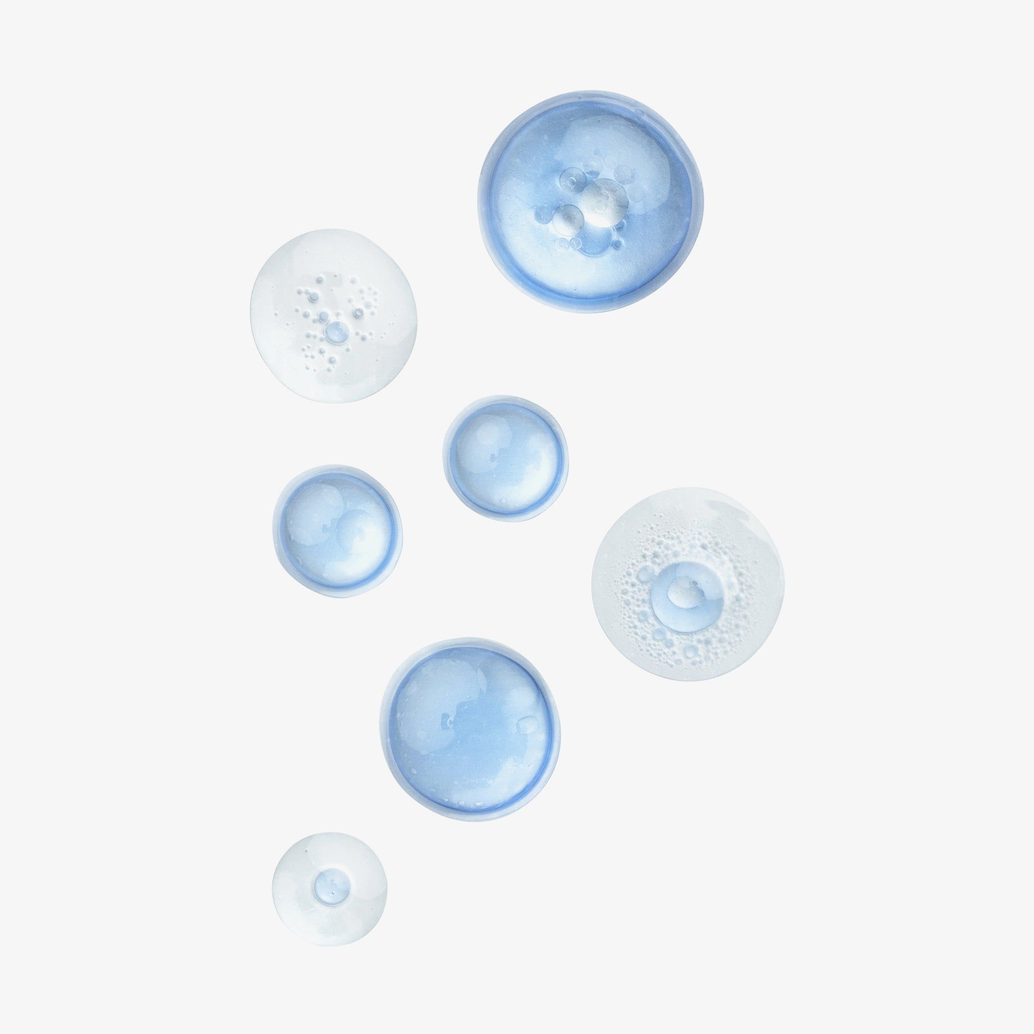 Mehrere blaue und transparente Tropfen auf weißem Hintergrund. Unterschiedliche Größen und Formen. Einige Tropfen sind schaumig.