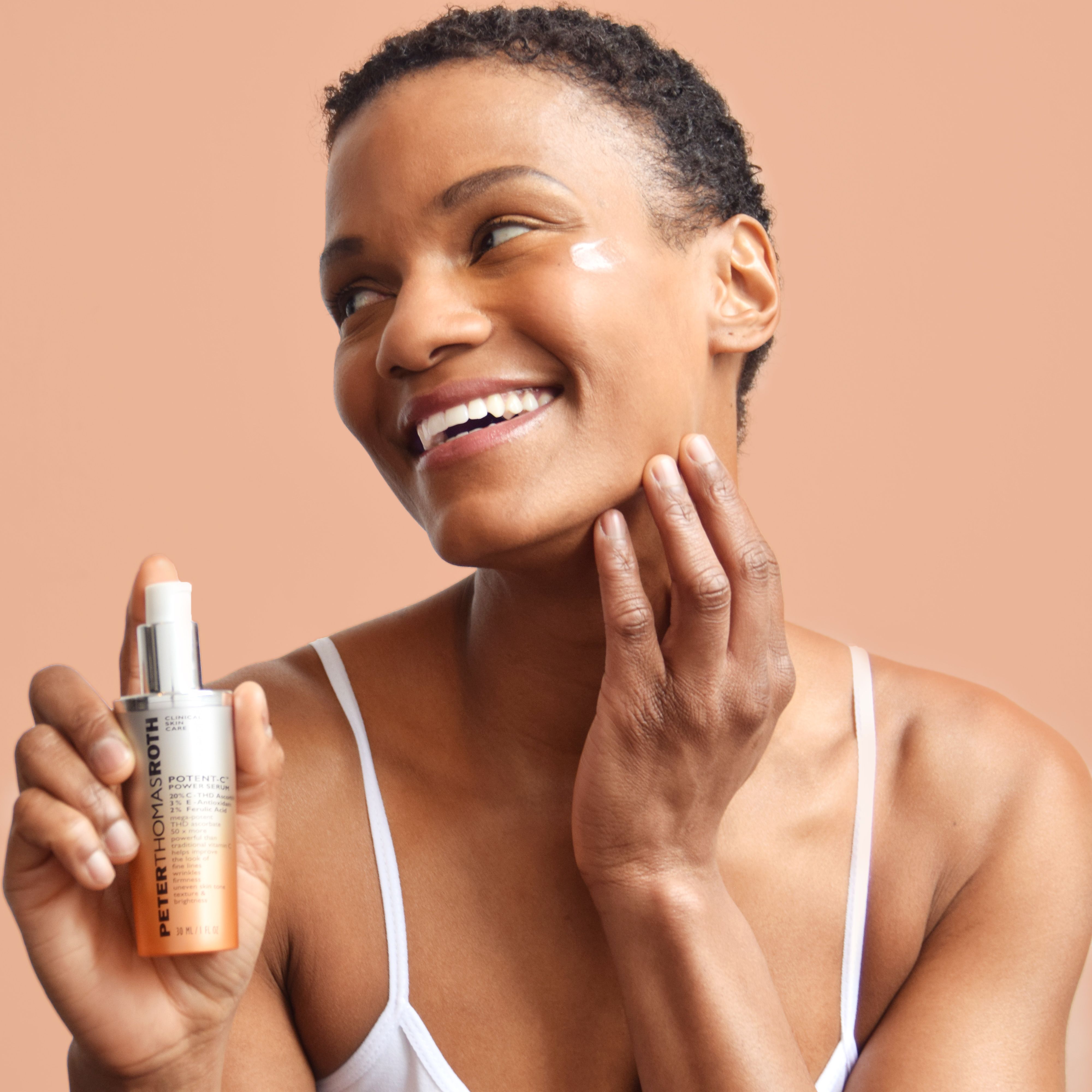 Frau hält Serumflasche. Aufschrift: Potent-C Power Serum. Silberne Kappe und orangefarbener Farbverlauf. Frau berührt Gesicht.