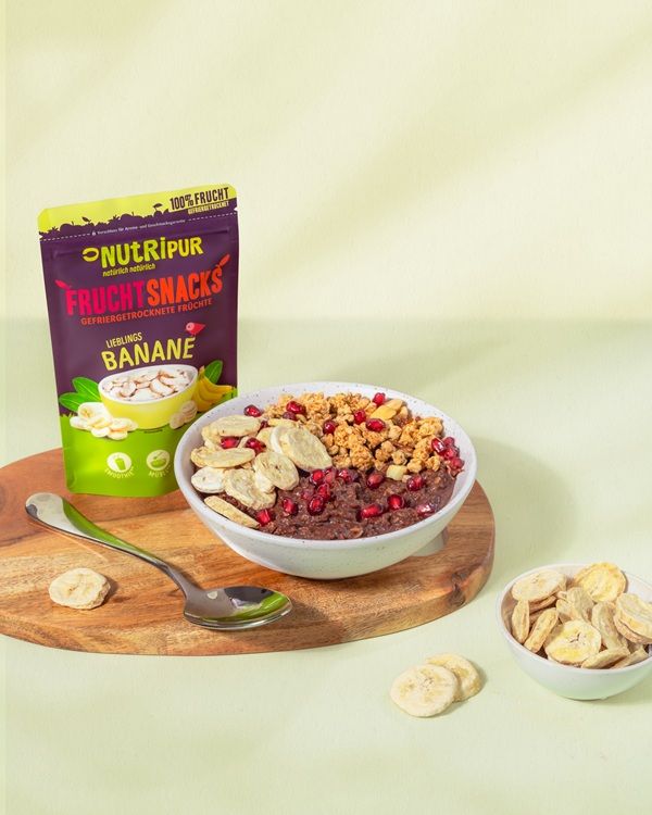 Produktpräsentation mit gefriergetrockneten Bananensnacks, einer Schüssel Müsli und einer Packung NutriPur Frucht Snacks.