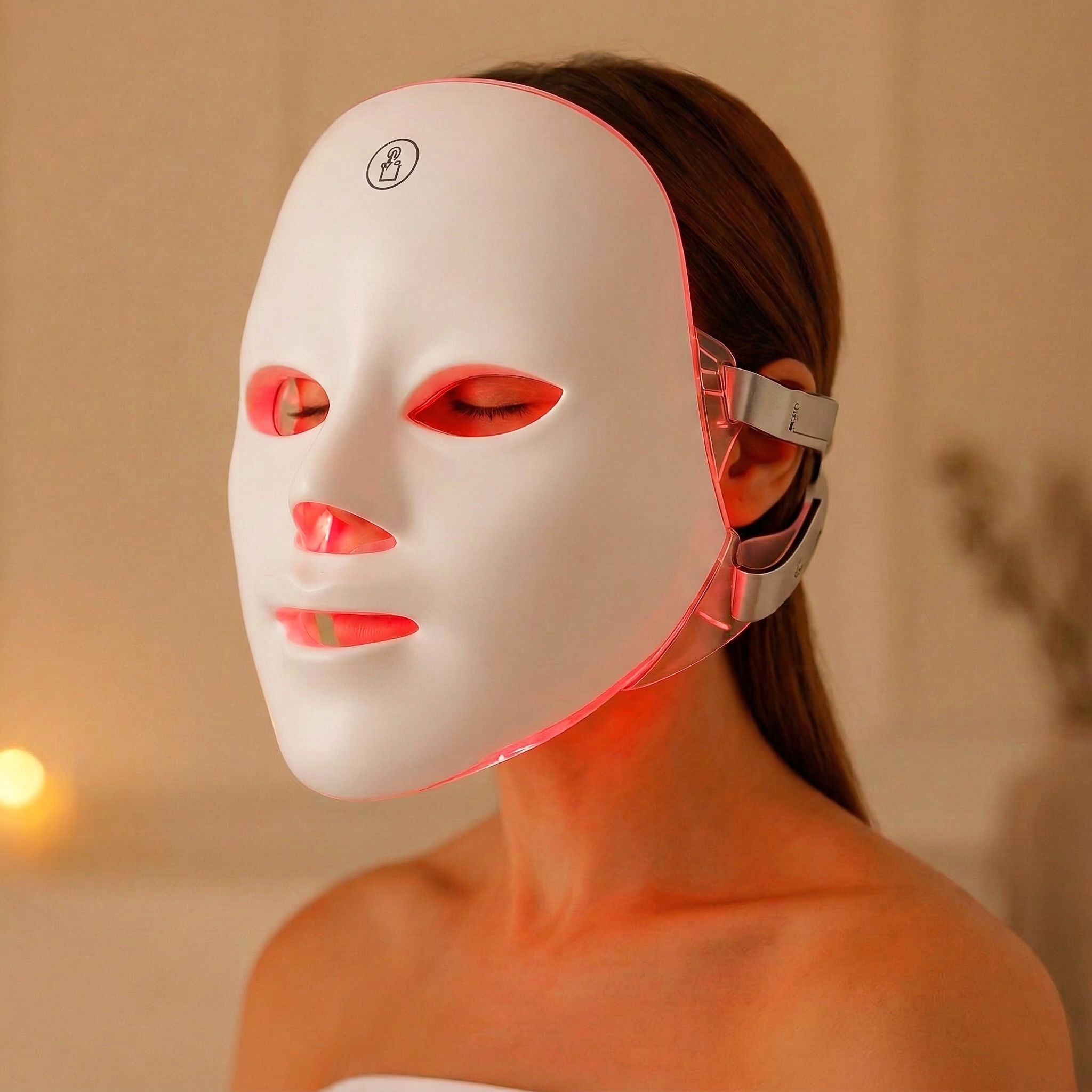 Weiße Gesichtsmaske mit roten Lichtern, getragen von einer Person. Seitliche Halterungen sind sichtbar.