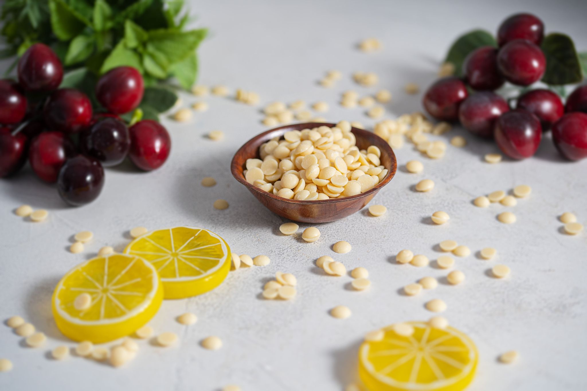 Weiße Schokodrops in einer braunen Schale, umgeben von Kirschen und Zitronenscheiben. Einige Drops sind verstreut.