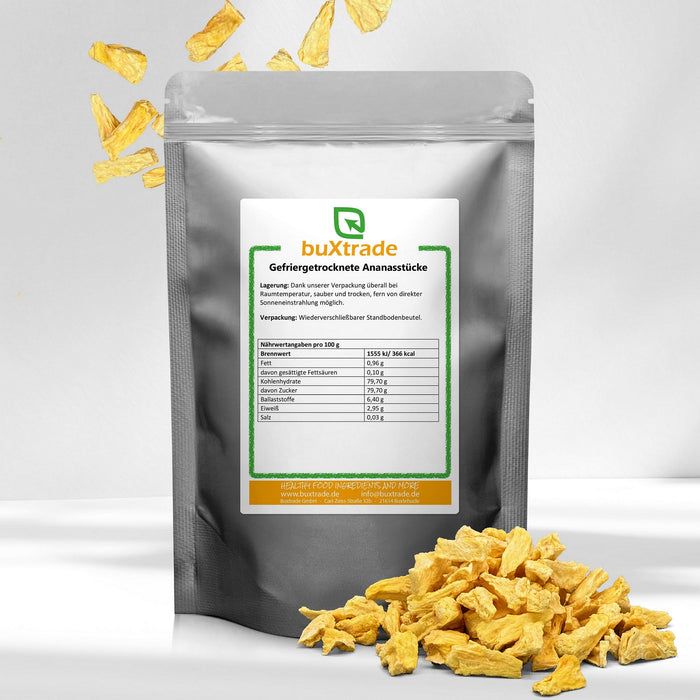 Silberne Tüte mit gefriergetrockneten Ananasstücken. Aufkleber mit Produktinformationen und Marke buXtrade. Einige Stücke liegen daneben.