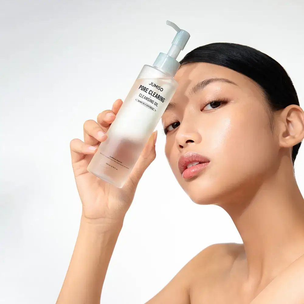 Frau hält eine Klarflasche mit Pumpe. Aufschrift: JUMISO PORE CLEARING CLEANSING OIL. Serum Control.