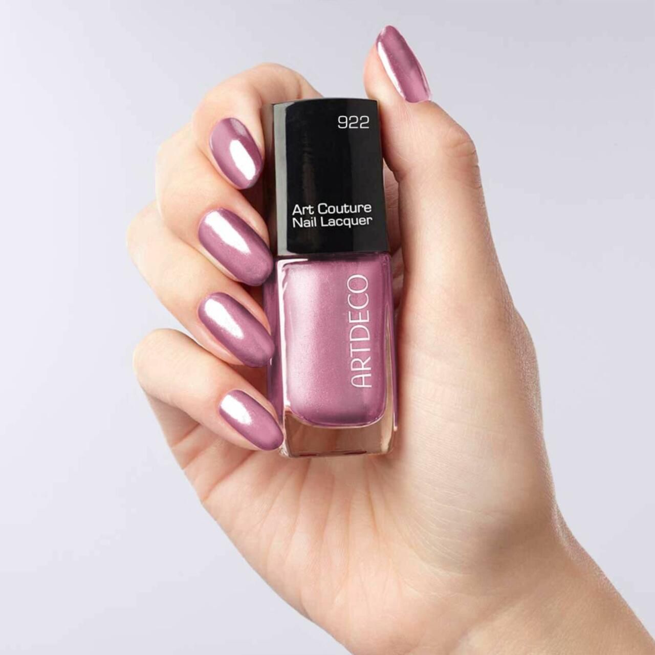 Hand hält eine Nagellackflasche und lackierte Nägel. Nagellackflasche mit Aufschrift Artdeco, Art Couture Nail Lacquer und 922.